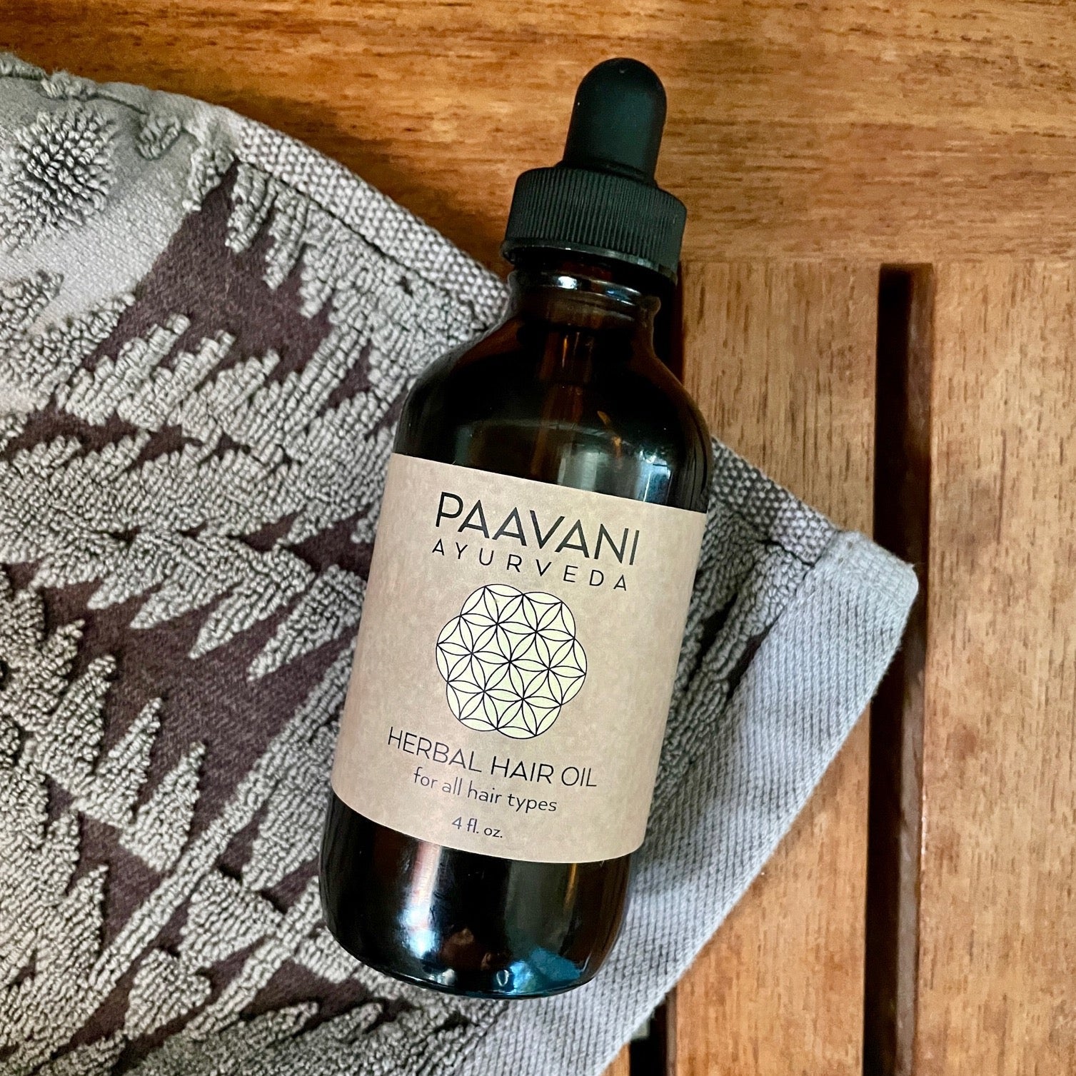 Ayurvedic Herbal Hair Oil bottle placed on a wooden tray with a towel – Luxurious self-care product for all hair types.