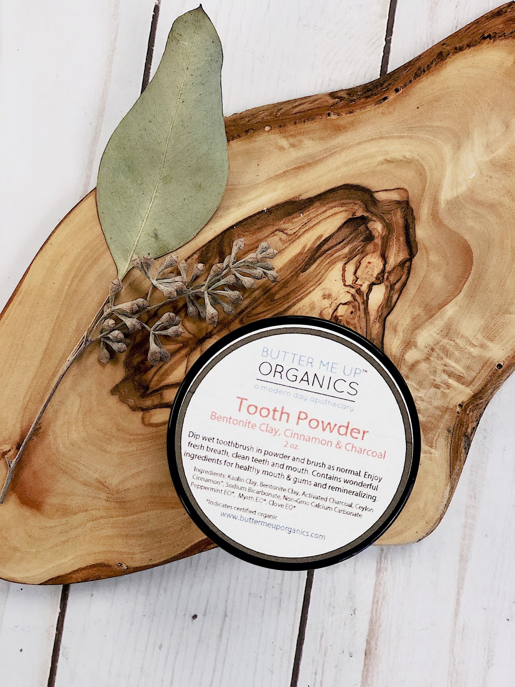 Close-up of Organic Tooth Powder jar with wooden accents and dried leaves for a natural aesthetic.