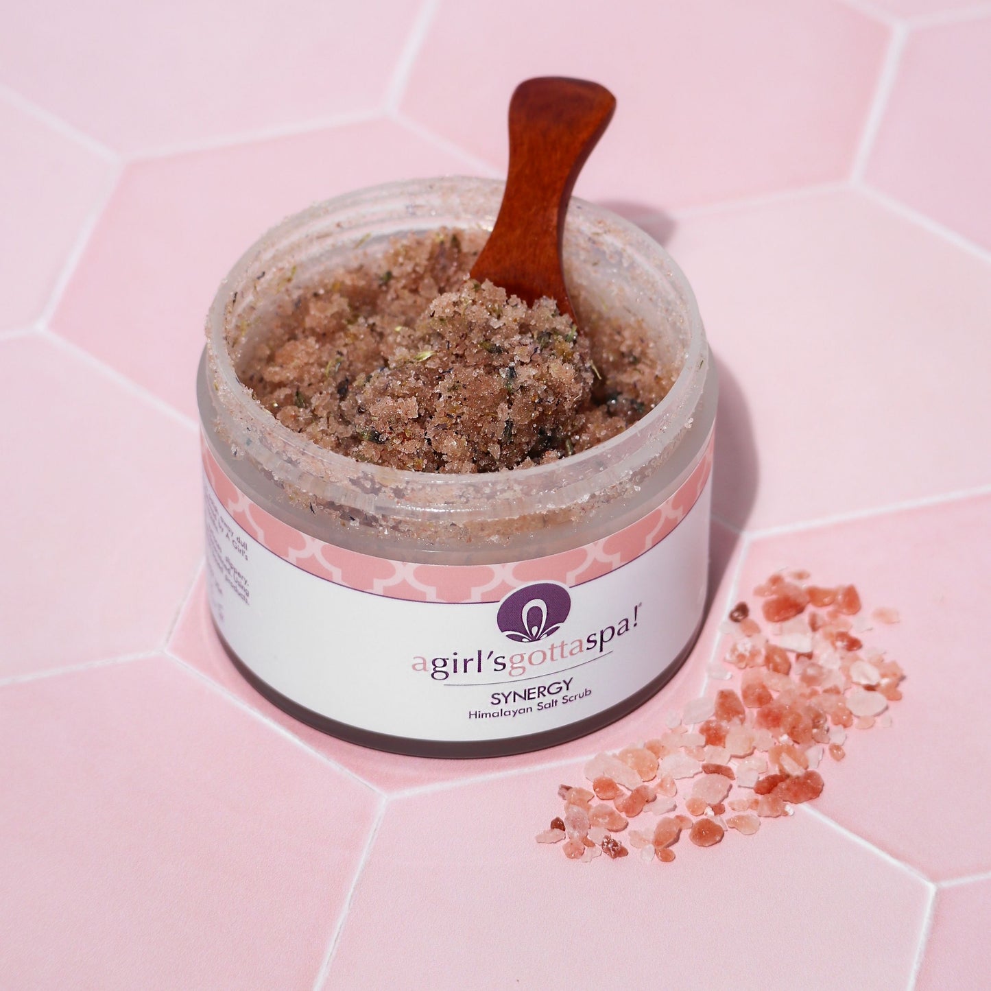 Synergy Himalayan Salt Body Scrub on pink background with wooden spoon – Aromatherapy and hydration in a jar.